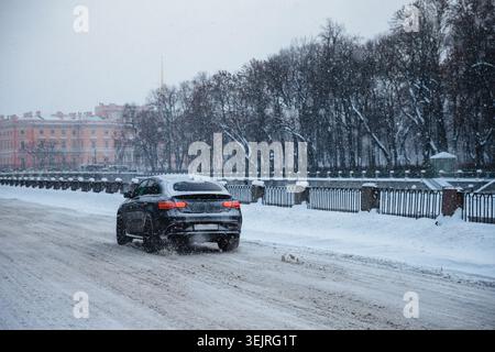 Black SUV drives on snowy city road during heavy winter snowfall near park Stock Photo