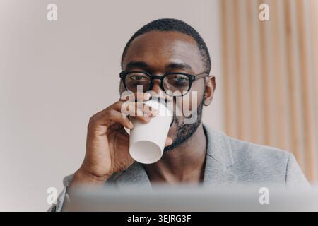 Businessman drinks coffee while working at laptop in modern office Stock Photo