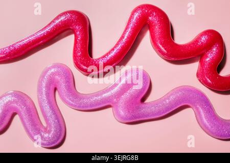 Glittering pink and purple cosmetic gels forming wavy lines on light background Stock Photo
