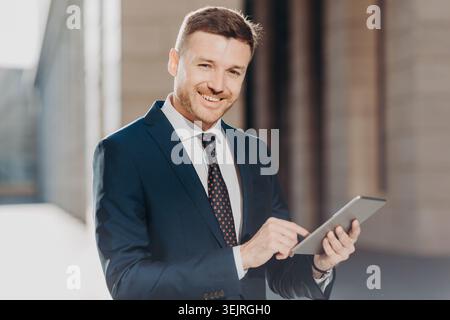 Smiling businessman uses digital tablet outside modern office building Stock Photo