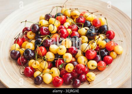 Assorted red yellow and dark cherries with stems on wooden plate Stock Photo