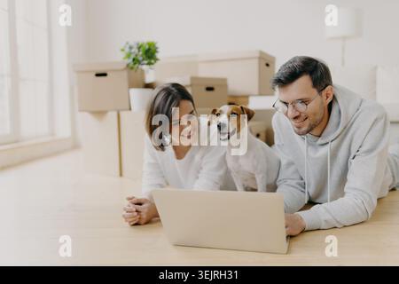 Young couple using laptop with Jack Russell terrier among moving boxes at home Stock Photo