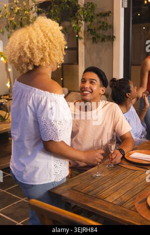 Standing woman leaning, starting toast celebrating during dinner, animated confetti marking flute. Friends, meal, intimate, convivial, lighting, decor Stock Photo