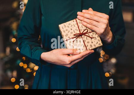 Woman holds wrapped Christmas gift with ribbon in festive indoor setting Stock Photo