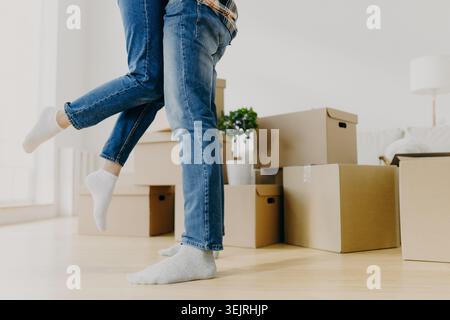 Couple jumps together beside cardboard boxes in bright new apartment Stock Photo