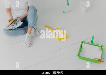 Person choosing paint color samples beside paint rollers on white wooden floor during home renovation Stock Photo