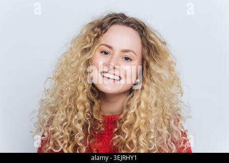 Smiling young woman with curly blonde hair poses for clean studio portrait Stock Photo