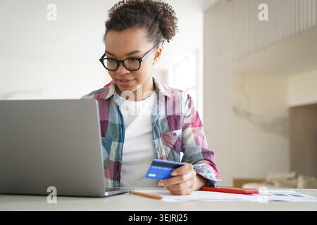 Young woman holding credit card and using laptop for online payment at home desk Stock Photo