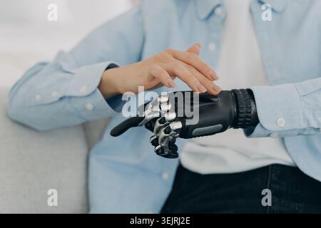 Person with bionic prosthetic hand touching robotic fingers while sitting indoors Stock Photo