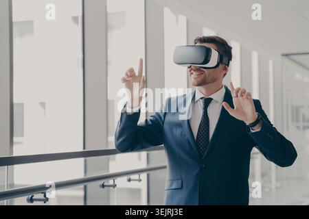 Businessman wearing virtual reality headset gestures in modern office corridor Stock Photo