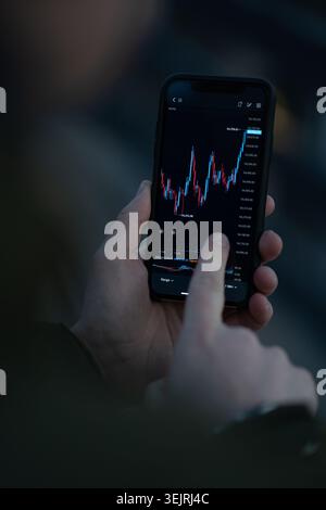 Person taps smartphone screen showing rising financial trading chart in low light Stock Photo