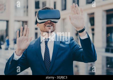 Businessman in suit using virtual reality headset while gesturing on city street Stock Photo