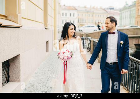 Bride and groom holding hands while walking together on historic city street after wedding ceremony Stock Photo