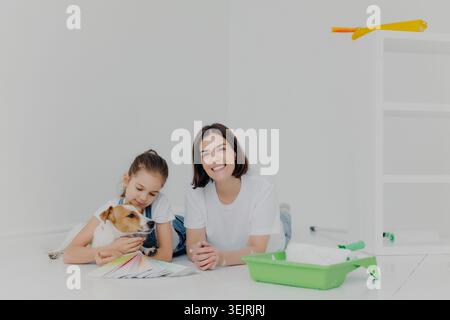 Mother and daughter choose paint colors with Jack Russell terrier in empty room during home renovation Stock Photo