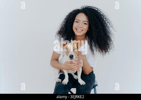 Young Black woman smiles while holding Jack Russell terrier dog in minimal studio Stock Photo