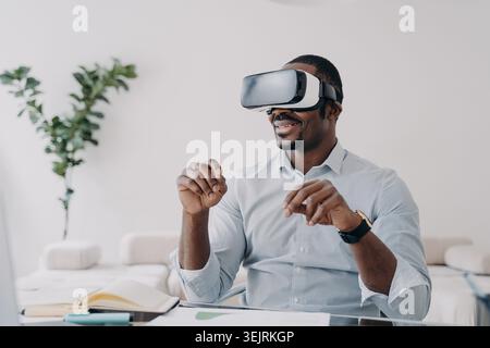 Man wearing virtual reality headset gestures with hands at desk in modern home office Stock Photo