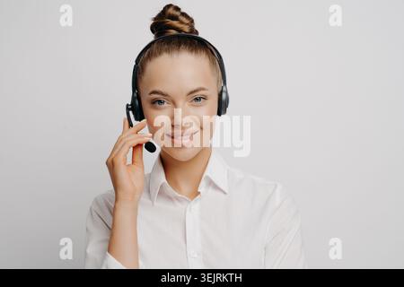 Young female customer service agent smiles while wearing headset against clean studio backdrop Stock Photo