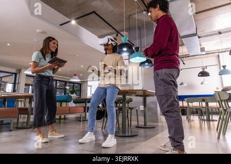 Diverse coworkers watching man wearing white VR headset gesturing near communal table with tablet Stock Photo