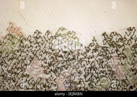 A green and brown military camouflage netting hangs against a light colored textured wall with a diamond grid wire pattern, fine cracks and covering t Stock Photo