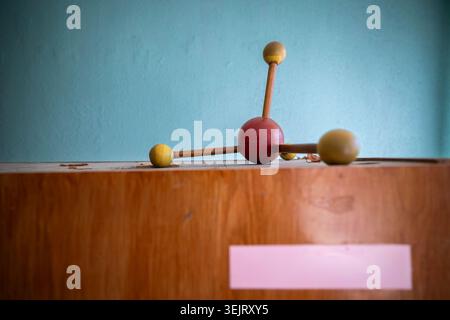 An old dusty wooden molecular model structure sits on top of a weathered wooden cabinet against a textured light blue painted wall inside an abandoned Stock Photo