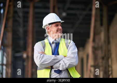Man, thinking and construction with arms crossed in city, foreman or supervisor with architecture mindset outdoor. Mature, contractor and happy with Stock Photo