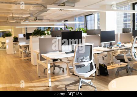 Modern office workspace featuring multiple desks with computers, ergonomic chairs, and plants, designed for productivity and collaboration in a bright Stock Photo