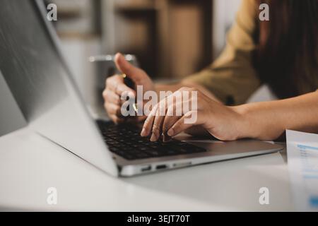 Young Asian woman working late at her desk, having a video call or online meeting with a laptop, analyzing data and managing business financials in an Stock Photo