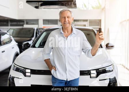 Happy mature customer standing in front of new SUV, holding car key Stock Photo