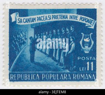 ROMANIA - 1951 September 22: 11 lei blue postage stamp depicting a mixed Musical Choir standing on a stage, performing under the direction of a conductor who faces them with raised arms. A large banner stretches across the top, while an emblem featuring a lyre and a peace dove with the year 1951 appears on the right. The historical context is the third World Festival of Youth and Students held in Berlin in 1951. The slogan translates to let us sing of peace and friendship between peoples, reflecting Soviet-backed Cold War peace propaganda designed to mobilize youth across the eastern bloc Stock Photo