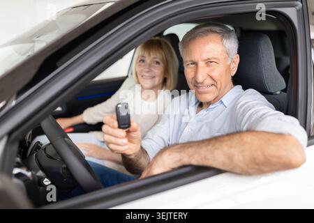Happy senior couple sitting inside new car at dealership, man holding key Stock Photo