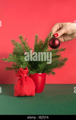 Womans hand decorates small red Christmas tree with gift bag. Close up. Xmas card. Holiday winter time. Stock Photo