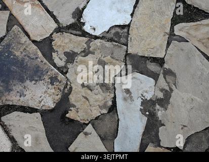 Horizontal close up of flat slate stone ground cover with multicolored porous uneven stones, black dirt between the stones, scattered dirt on top Stock Photo