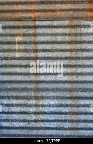 Vertical close up of weathered corrugated galvanized metal siding with horizontal ridges, overlapping panels, rust streaks Stock Photo