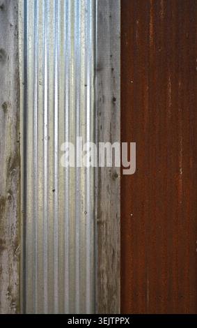 Weathered silver corrugated tin panel and heavily rusted reclaimed tin panel with vertical wood boards showing wood grain, knots, seams Stock Photo