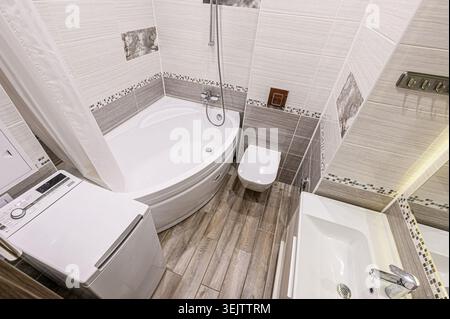 interior apartment Modern, compact bathroom with white bathtub, toilet, and shower.  Neutral grey and white tile, minimalist design. Clean lines and s Stock Photo