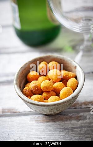 Spicy nuts in a ceramic dish; a bottle of beer in background. Bright wooden background. Close up. Stock Photo