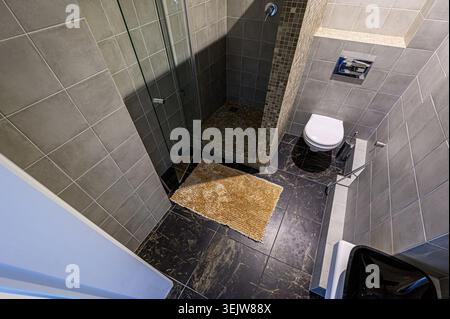 Modern, sleek bathroom with gray tile, glass shower enclosure, black sink, and compact toilet.  Marble-like flooring adds a touch of luxury. Minimalis Stock Photo