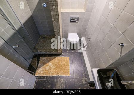 Modern, sleek bathroom with gray tile, glass shower enclosure, black sink, and compact toilet.  Marble-like flooring adds a touch of luxury. Minimalis Stock Photo
