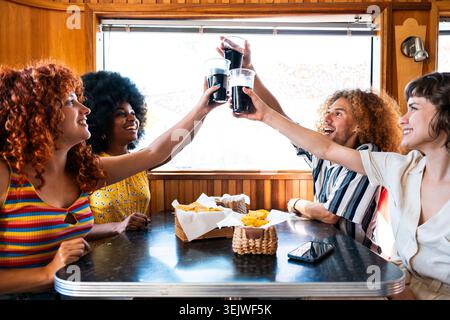 Multiethnic group of young happy friends bonding at vintage diner burger house restaurant - young diverse people bonding and celebrating together in a Stock Photo