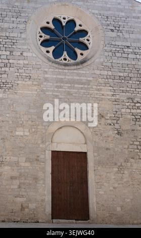 A timeless view of the textured stone exterior of St. Dominic's Church, showcasing a detailed gothic rose window above a closed wooden arched door. Stock Photo