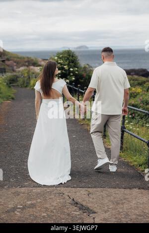 Couple walks hand in hand along seaside path Stock Photo