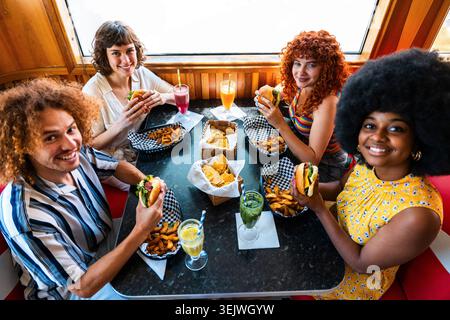 Multiethnic group of young happy friends bonding at vintage diner burger house restaurant - diverse group of smiling friends happily eating fast food Stock Photo