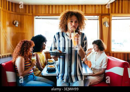 Multiethnic group of young happy friends bonding at vintage diner burger house restaurant - diverse friends bonding, eating burgers and drinking bever Stock Photo