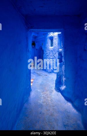 Blue Medina passage in Chefchaouen shows a narrow painted stairway and textured walls glowing under cool interior light. Stock Photo