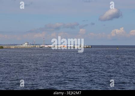 Clouds drift above the tranquil sea. The pier extends into gentle waves. Water reflects the sky's soft hues. Perfect for maritime travel or coastal sc Stock Photo
