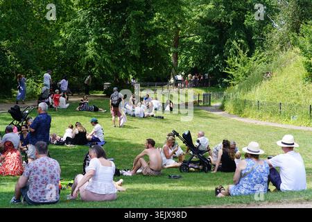 People relaxing and picnicking on green grass in sunny park on beautiful summer day, families enjoying outdoor leisure under leafy trees.Tonbridge Stock Photo