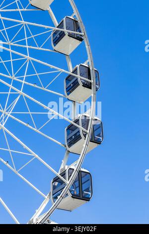 Ferris wheel cabins and geometric framework against vibrant blue sky background Stock Photo