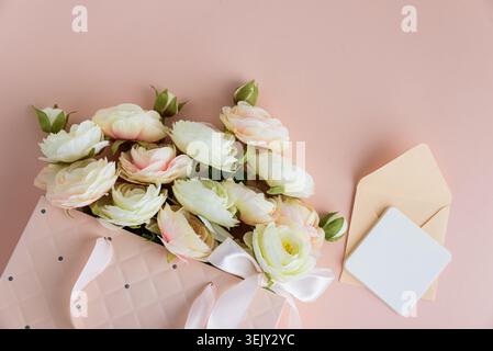 Festive composition featuring a quilted pink gift bag filled with cream and blush artificial rose flowers, accented by a white ribbon bow and gift car Stock Photo