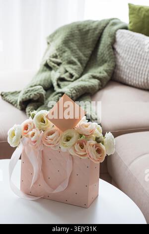 Delicate lifestyle composition featuring a quilted pink gift bag filled with cream and blush ranunculus flowers, accented by ribbon handles and decora Stock Photo