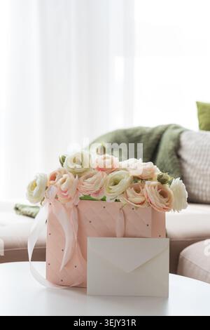 Delicate lifestyle composition featuring a quilted pink gift bag filled with cream and blush ranunculus flowers, accented by ribbon handles and decora Stock Photo